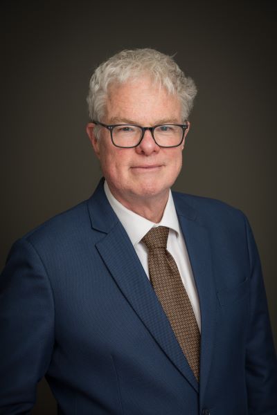 A staff profile image of Robert Hay wearing a blue suit with a brown tie. 