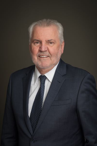 A profile image of Gary Arnold wearing a dark blue suit with a white collared shirt and dark blue tie. 